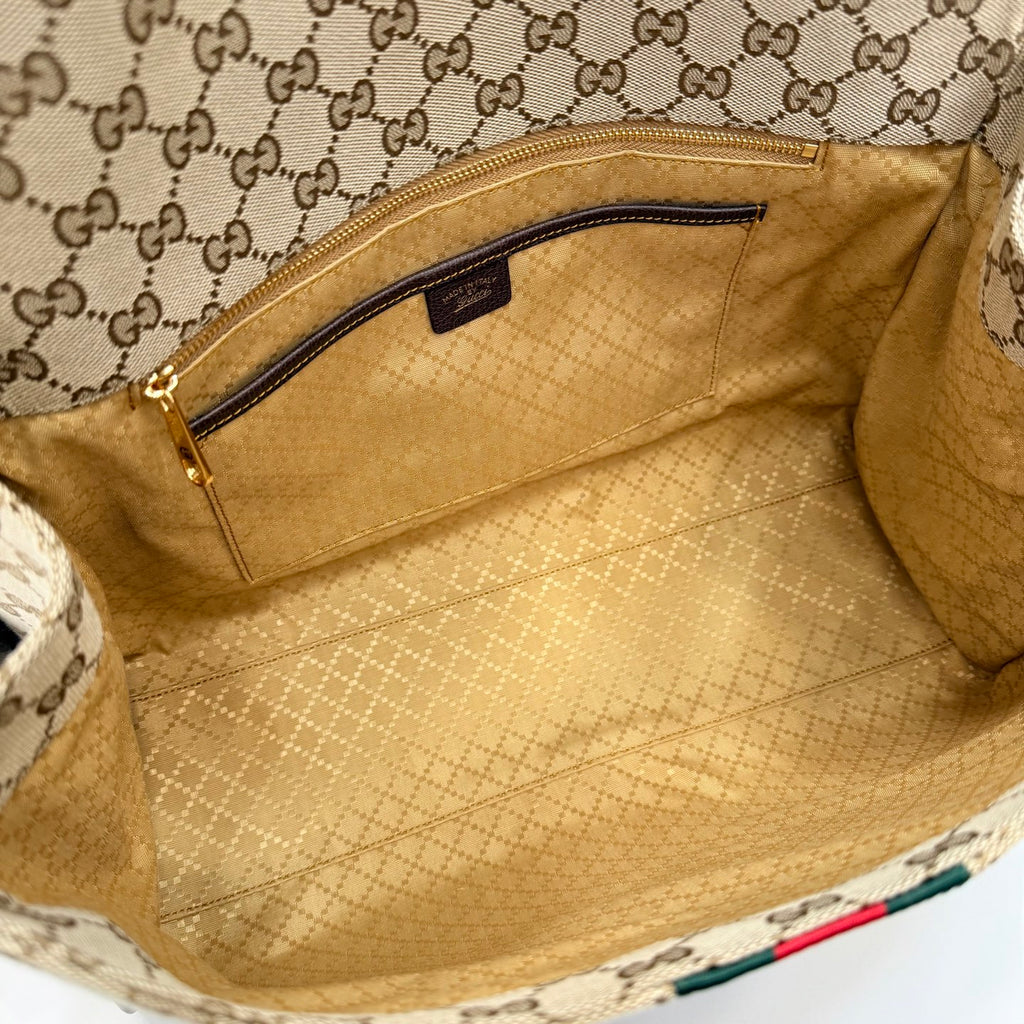 Interior of GG-print bag with beige lining and zippered pocket, open top view