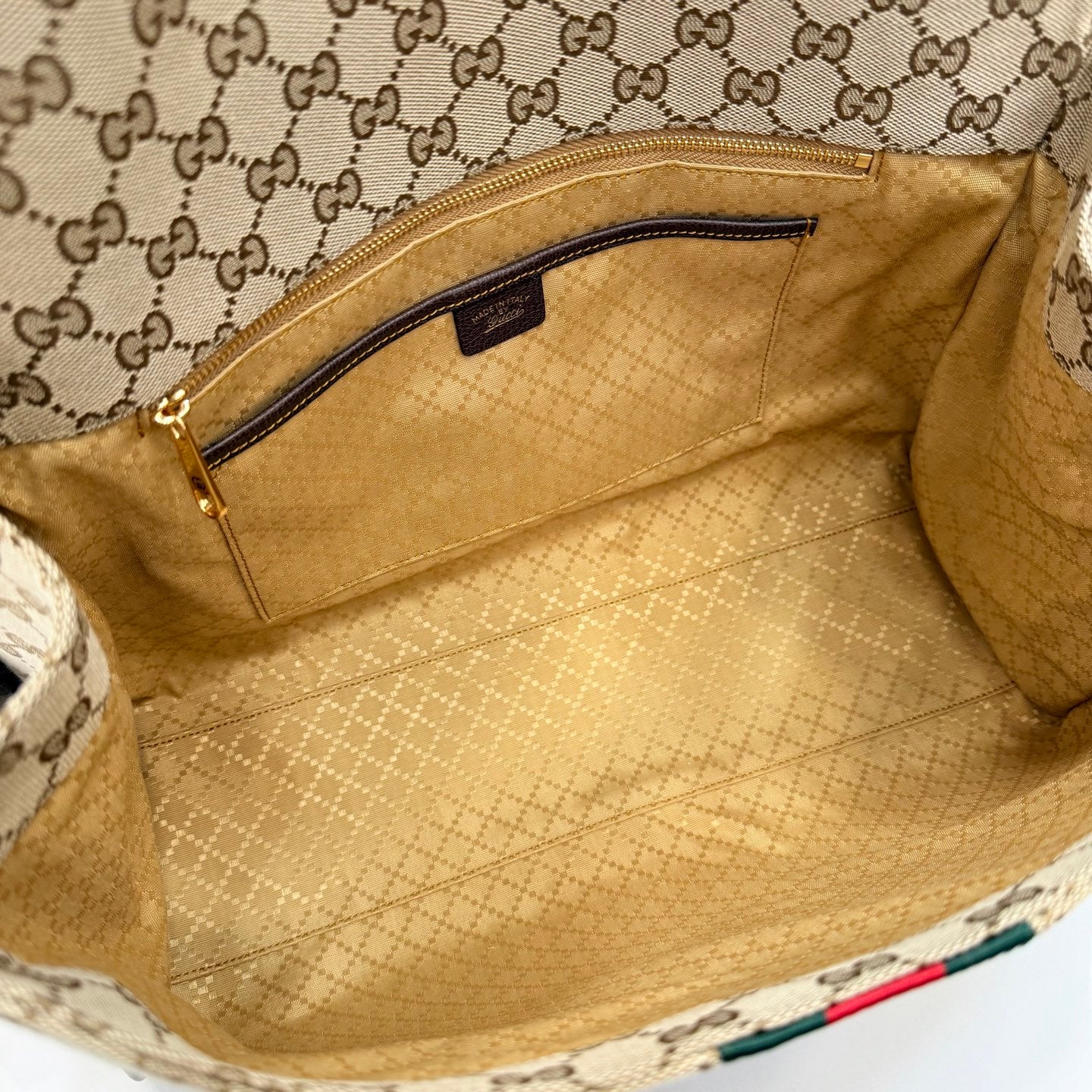Interior of GG-print bag with beige lining and zippered pocket, open top view