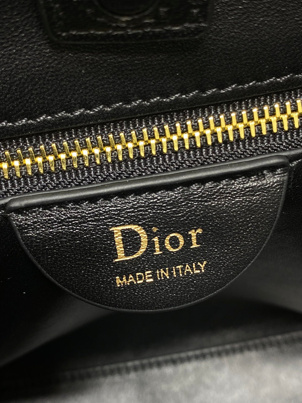 Dior zipper pull with 'Made in Italy' and gold teeth on dark leather bag.