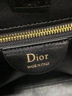 Dior zipper pull with 'Made in Italy' and gold teeth on dark leather bag.
