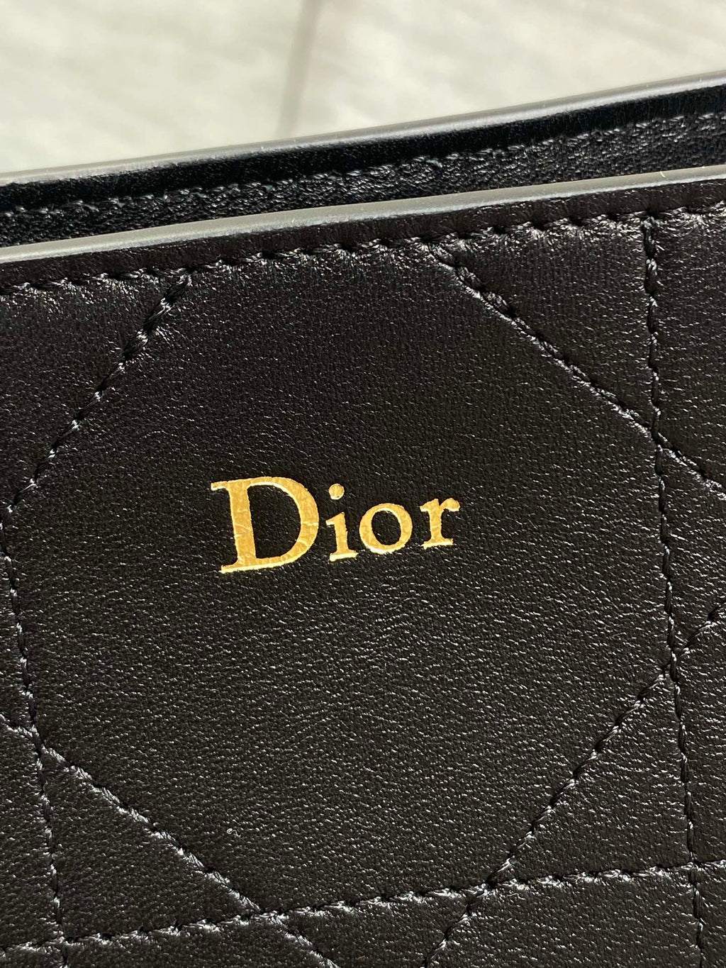 Dior logo patch on dark quilted leather bag front, stitched diamond pattern.