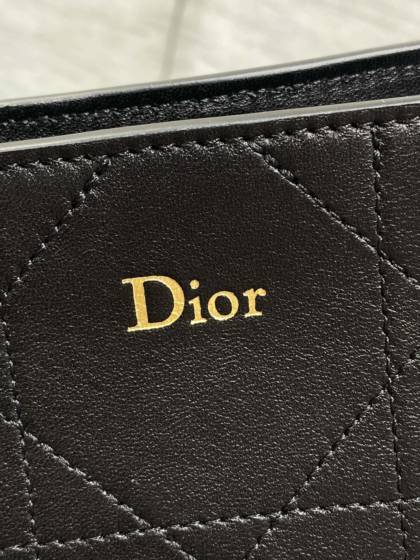 Dior logo patch on dark quilted leather bag front, stitched diamond pattern.