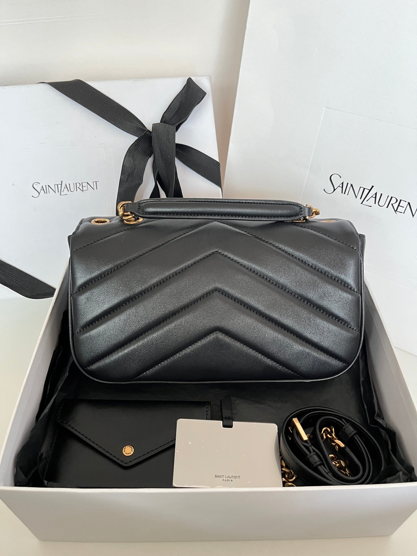 Dark gray leather YSL bag with chevron quilting, gold emblem, and short shoulder strap.