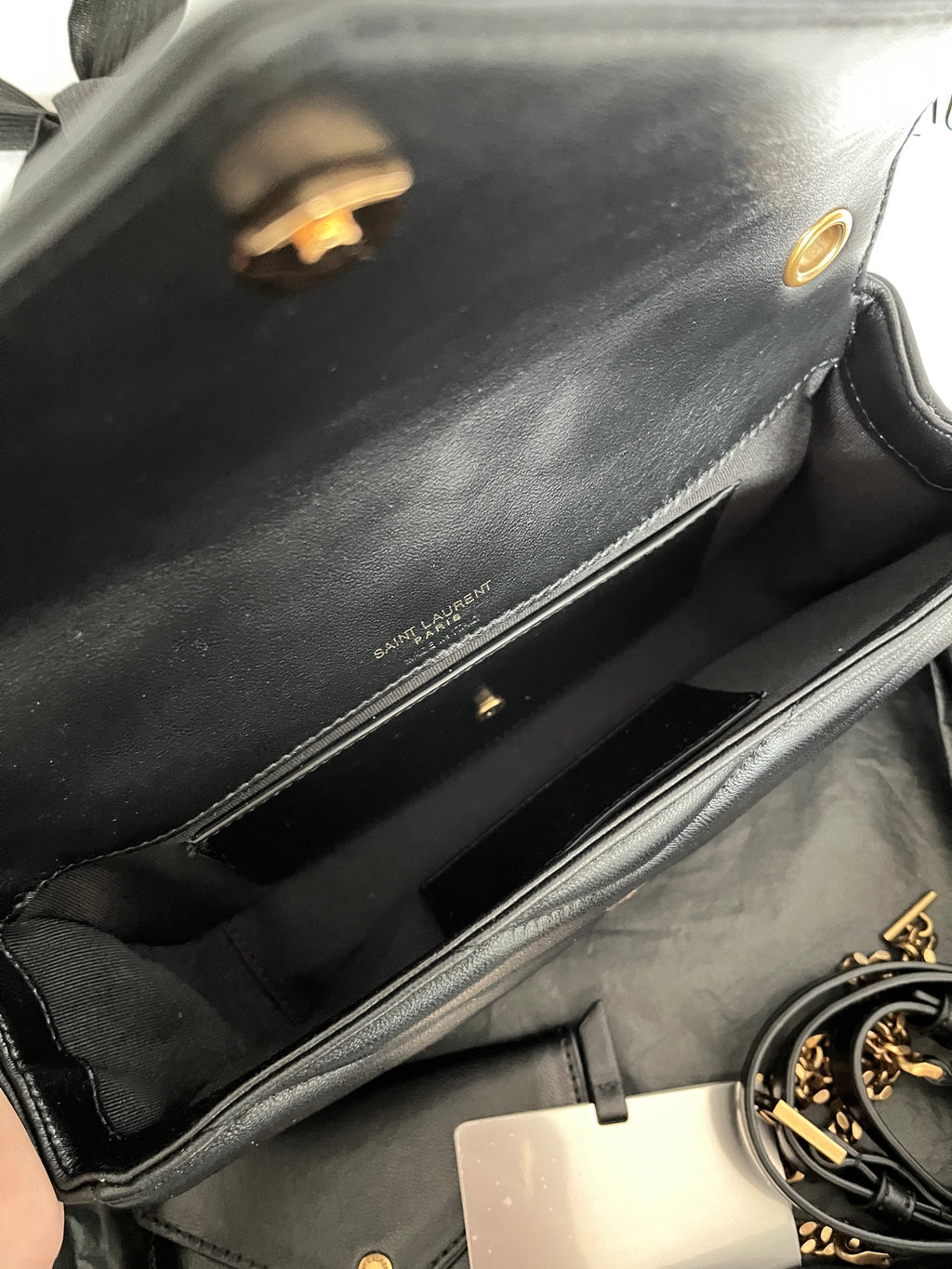 Dark gray leather YSL bag interior with gold snap flap, zipper trim, and logo stamp.