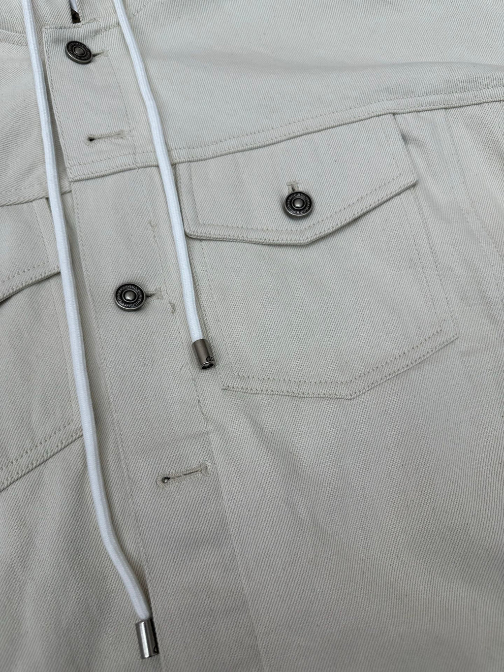 White jacket detail: snap placket, buttoned chest pocket and drawstring cords