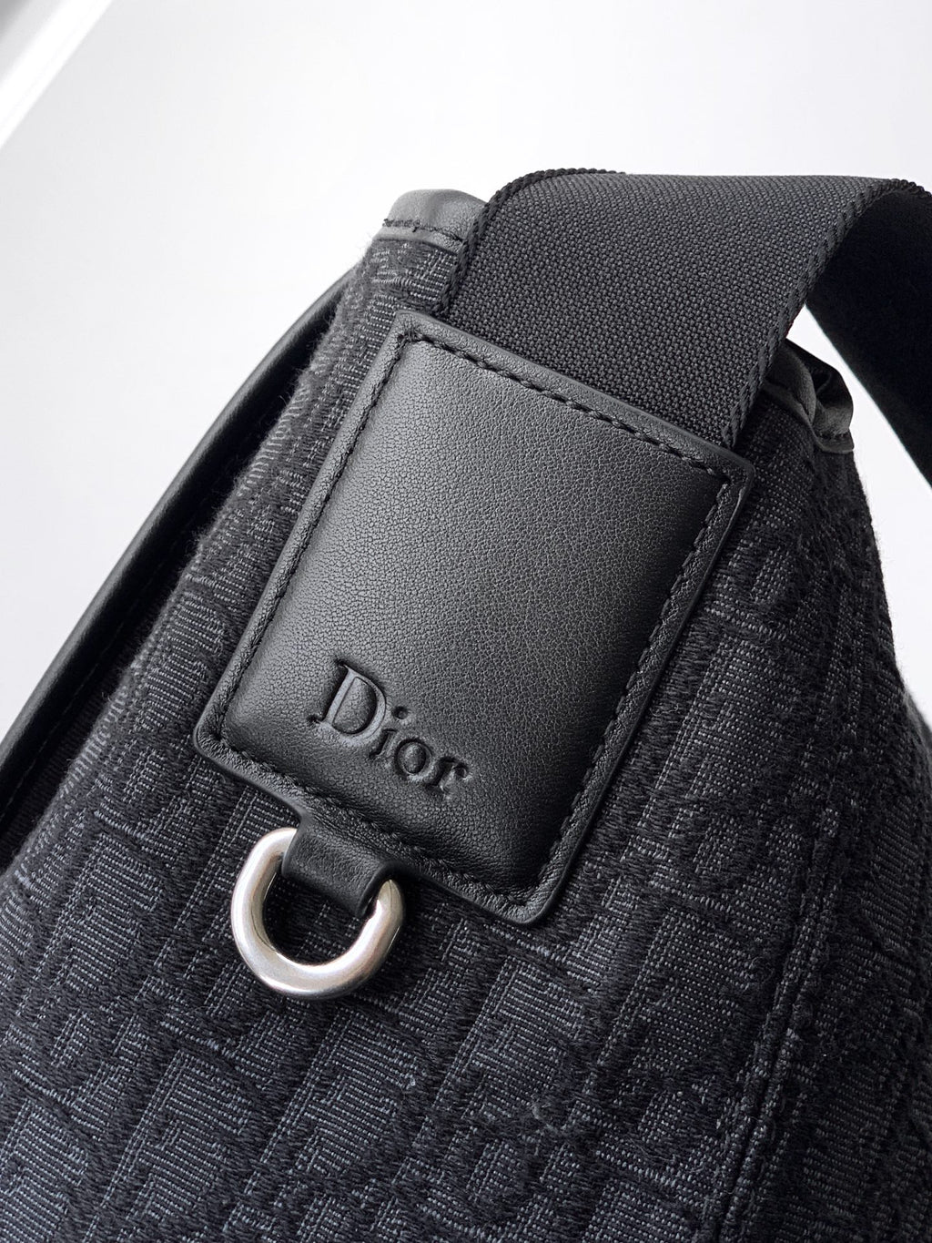 Dior bag front patch with Dior text and silver O-ring on dark navy textile