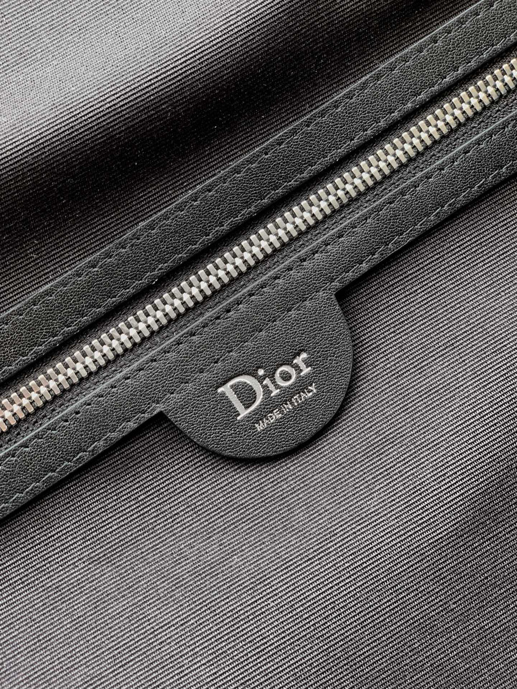Dior bag close-up of black leather patch with Dior logo and silver zipper