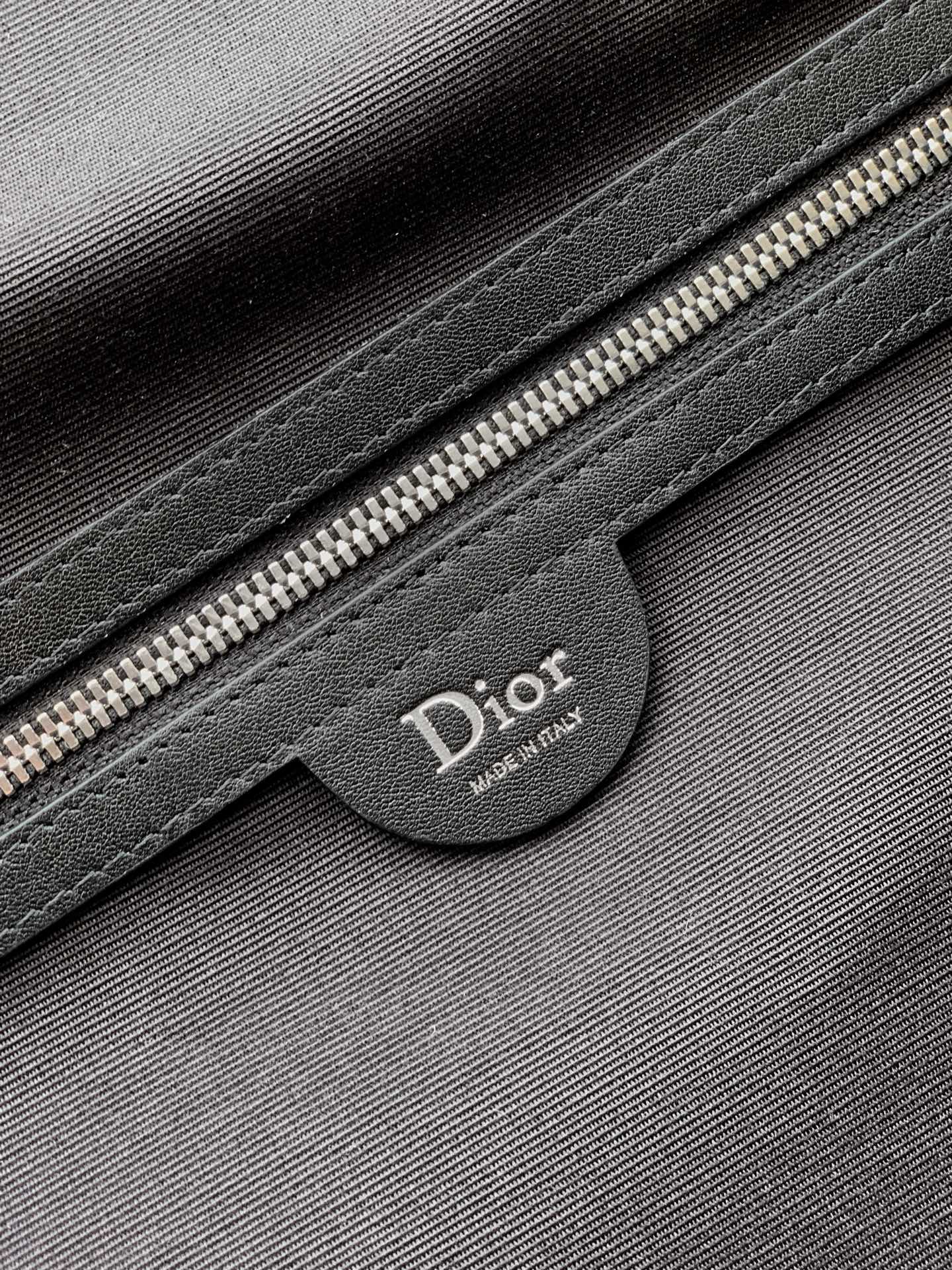 Dior bag close-up of black leather patch with Dior logo and silver zipper