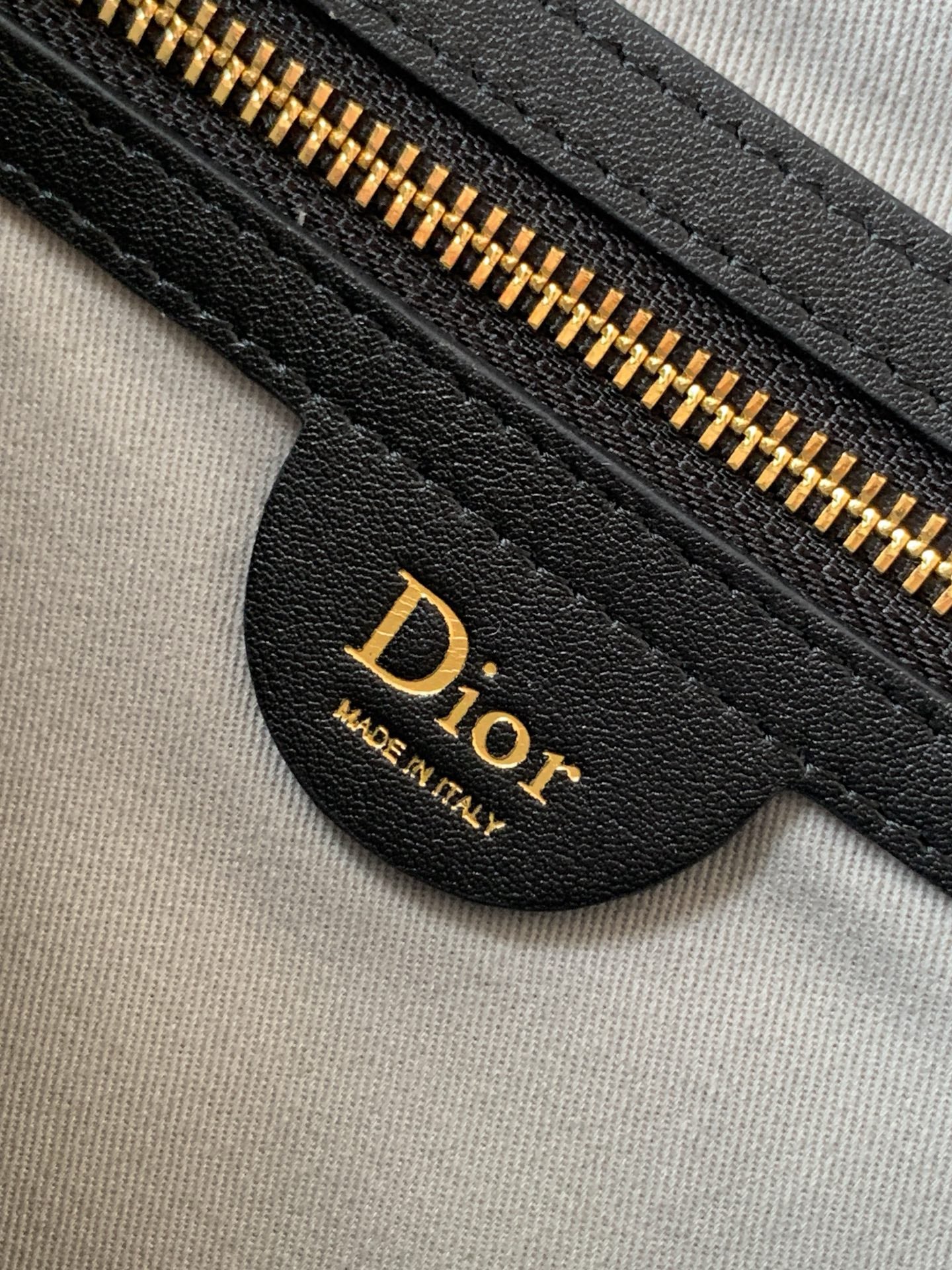 Dior bag detail: black leather logo patch with gold-tone zipper and pull tab