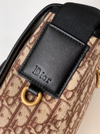 Dior bag detail: black leather front patch with Dior logo on beige patterned canvas