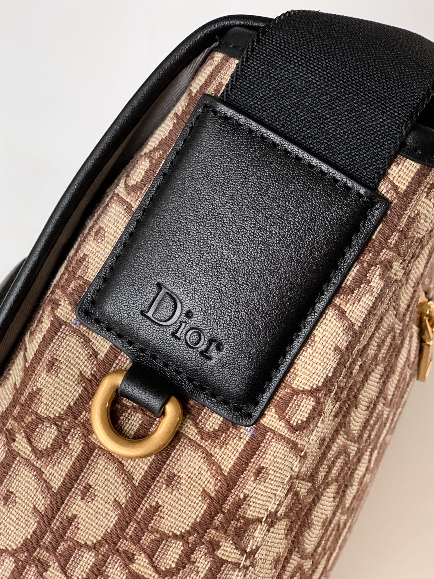 Dior bag detail: black leather front patch with Dior logo on beige patterned canvas