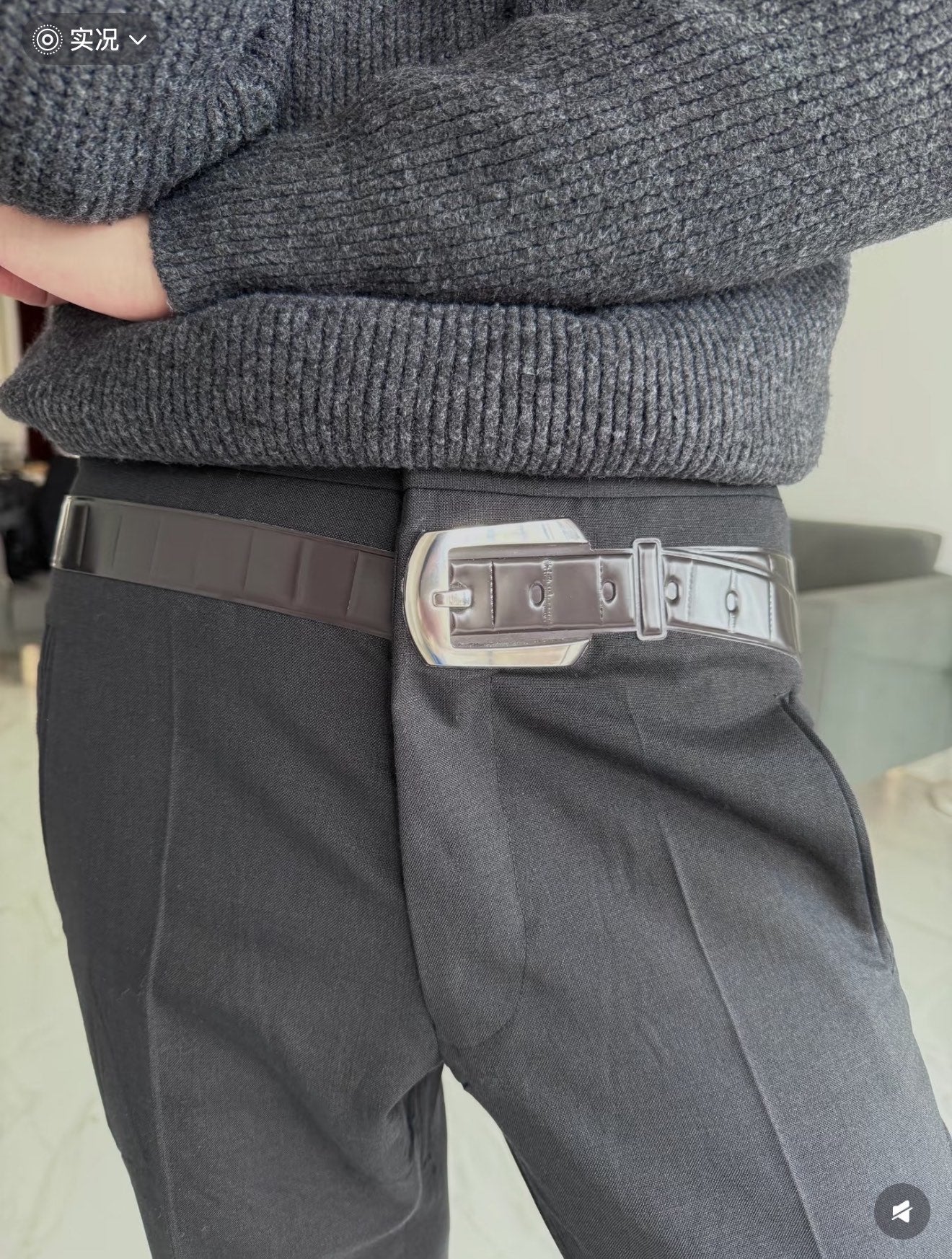 Dark gray pants with pleats and adjustable belt; straight-leg fit
