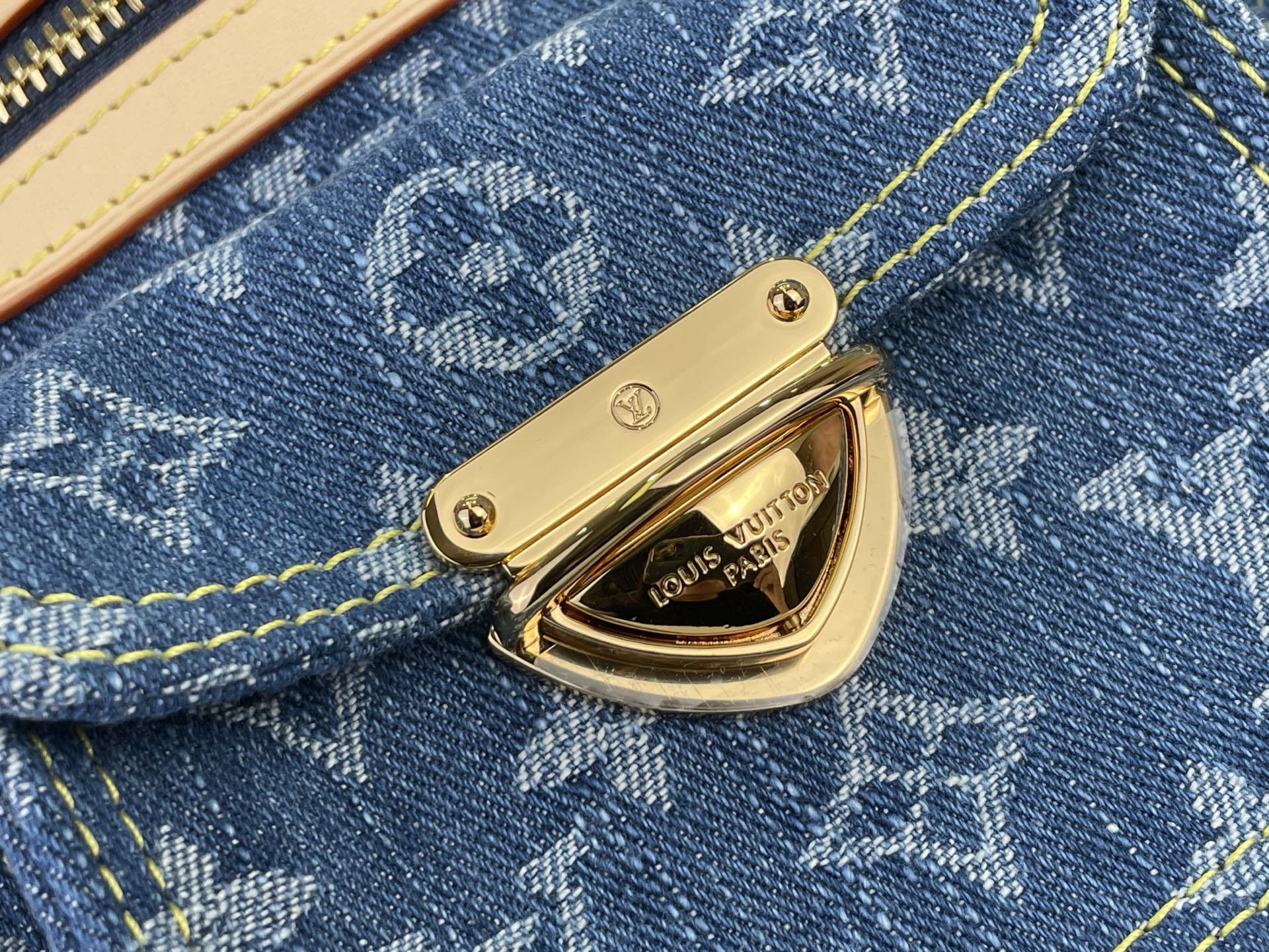 Gold front clasp on blue monogram denim flap pocket with yellow stitching
