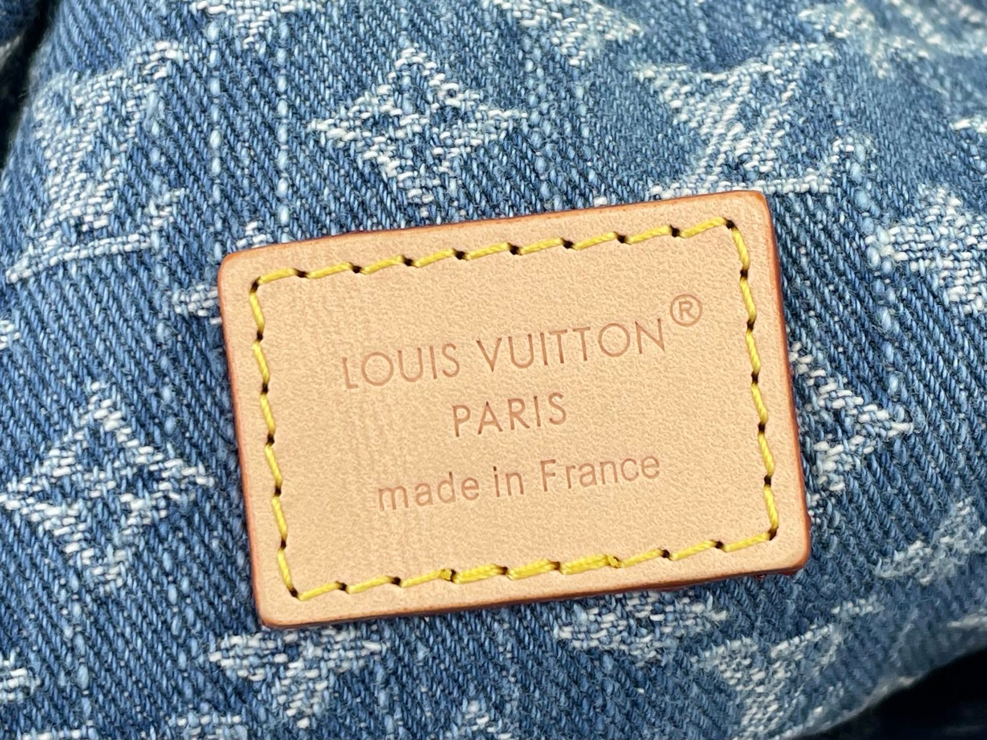 Tan leather brand patch on blue monogram denim bag with stitched border