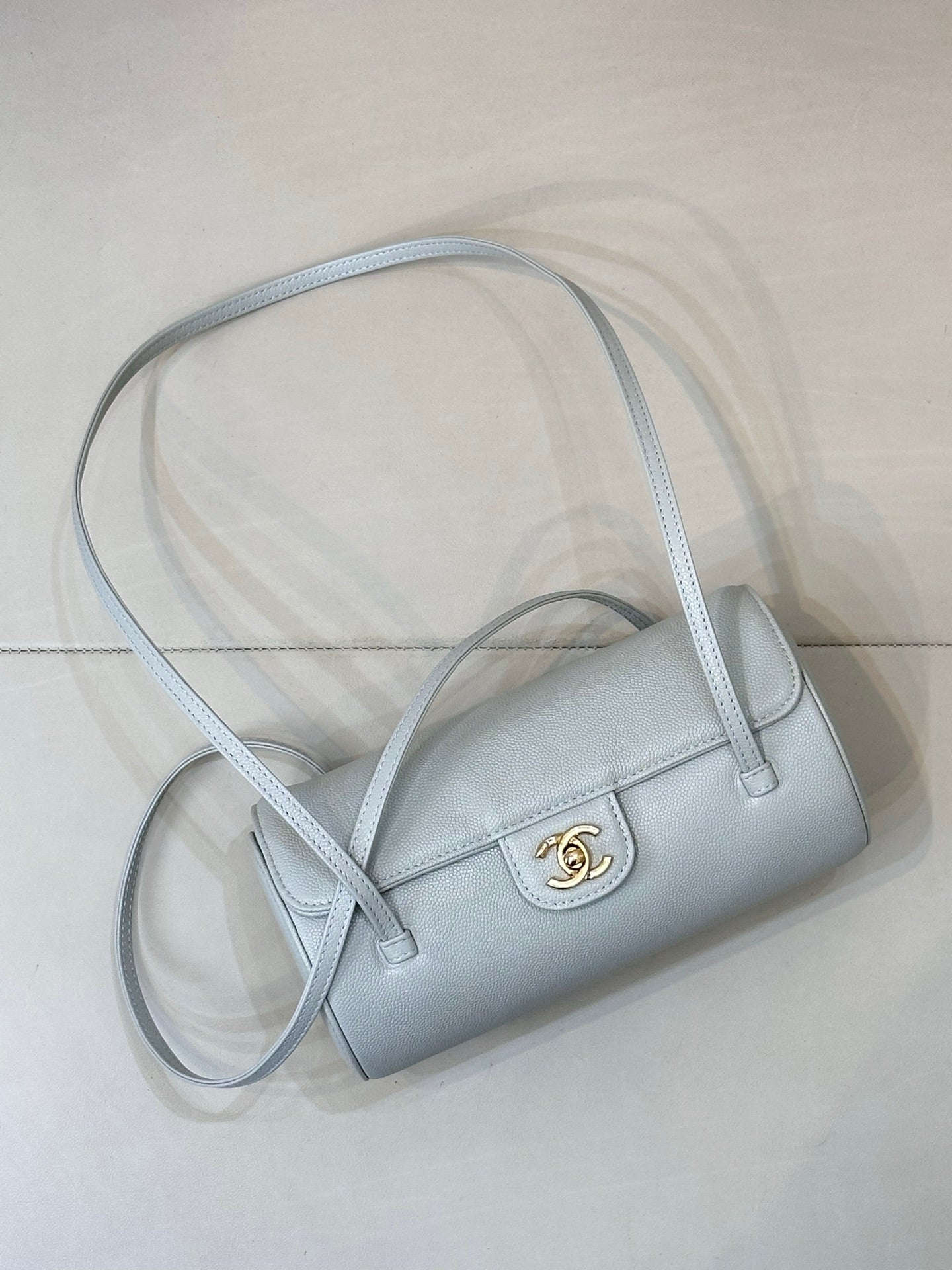 Light blue Chanel handbag with top handle and long crossbody strap, gold logo clasp