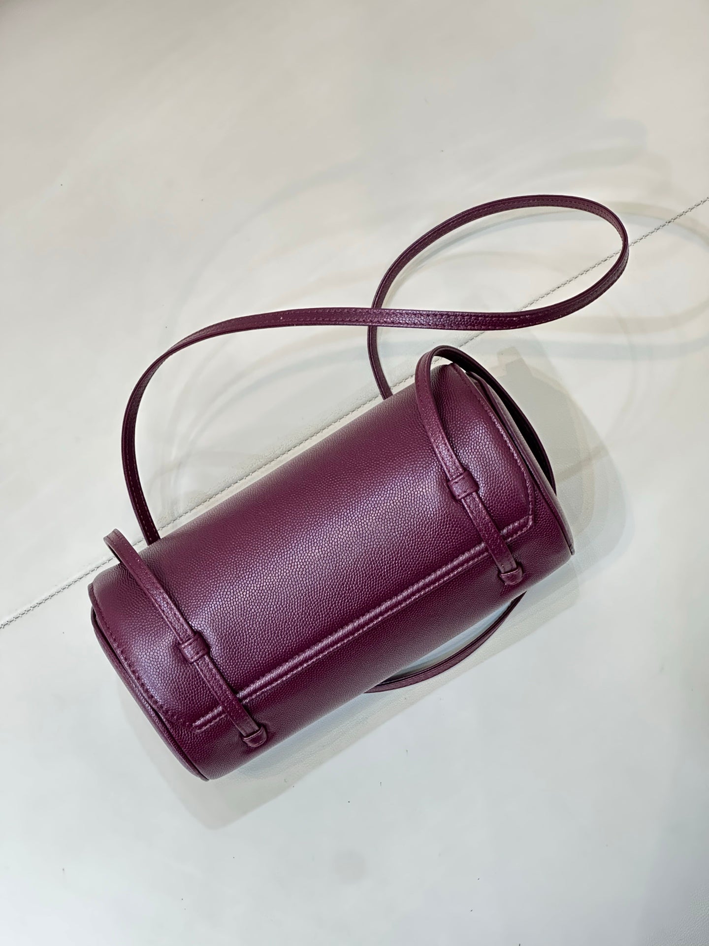 Burgundy leather cylindrical mini bag with structured top handle and crossbody strap
