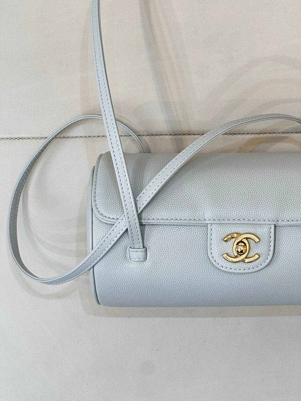 Light blue Chanel handbag close-up with gold logo on front and long crossbody strap