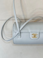Light blue Chanel handbag close-up with gold logo on front and long crossbody strap