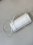 Chanel white leather cylindrical handbag with strap, stitched seams, and gold hardware.