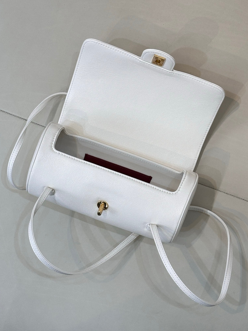 Chanel white leather handbag open view with burgundy interior lining and gold clasp.