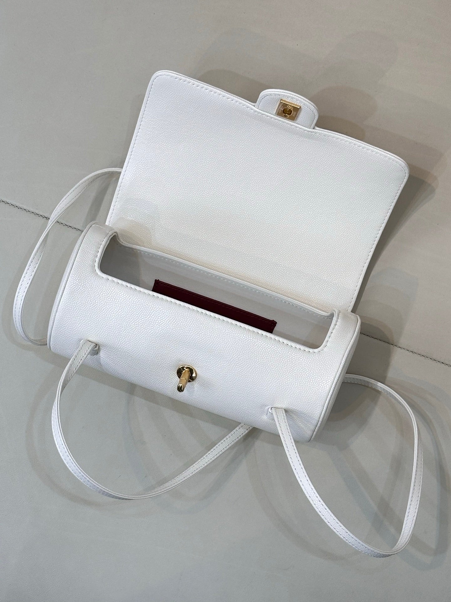 Chanel white leather handbag open view with burgundy interior lining and gold clasp.