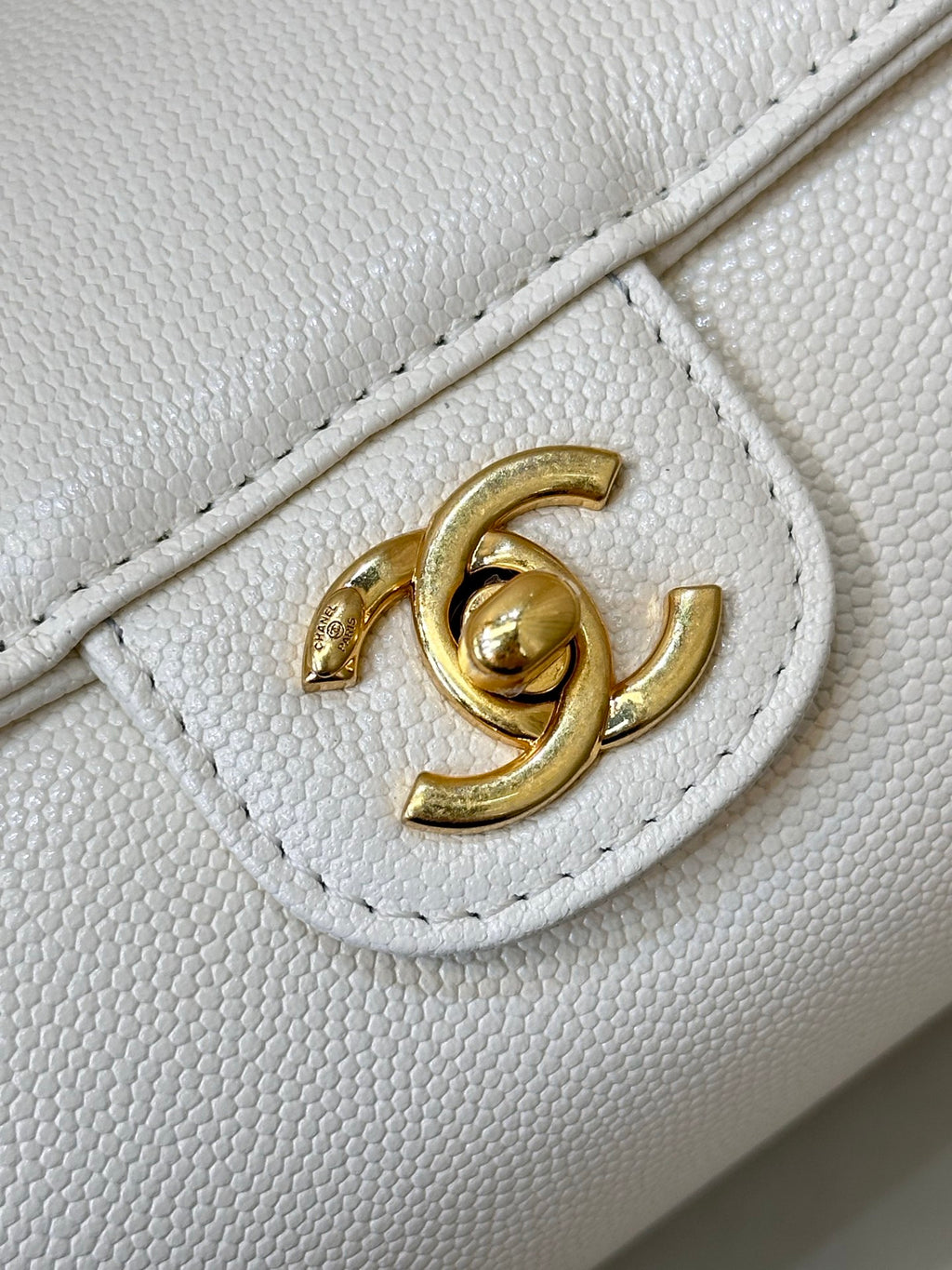 Chanel white leather bag close-up of gold CC turn-lock on front flap.