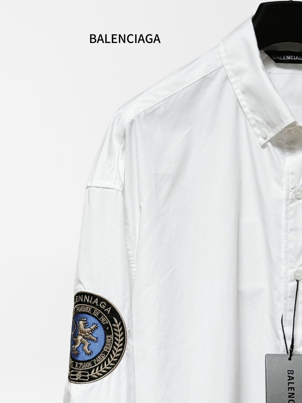 Balenciaga long-sleeve shirt shoulder detail, white fabric with round blue sleeve patch.
