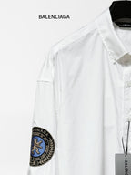 Balenciaga long-sleeve shirt shoulder detail, white fabric with round blue sleeve patch.