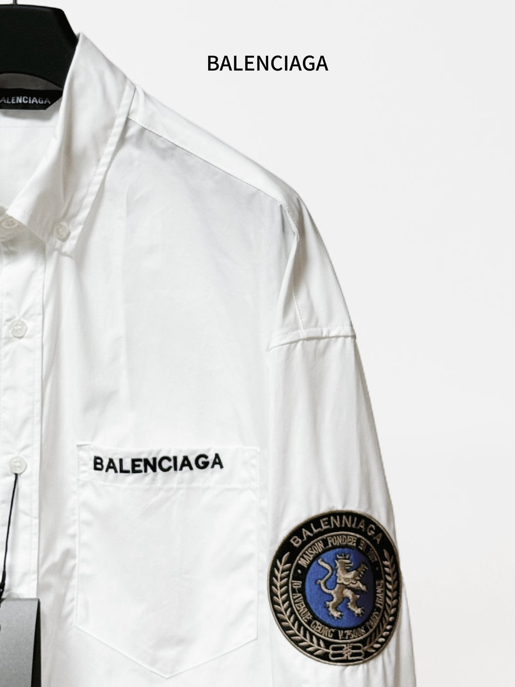 Balenciaga long-sleeve shirt close-up, white, with front logo and round sleeve patch.