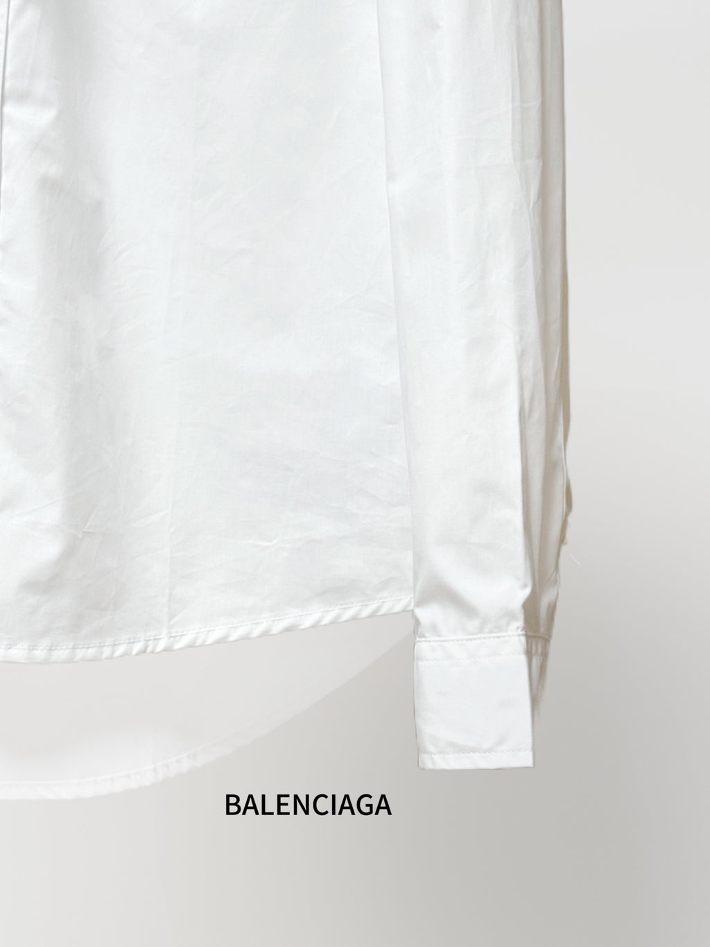 Balenciaga long-sleeve shirt lower back, white fabric with curved hem and sleeve cuff.