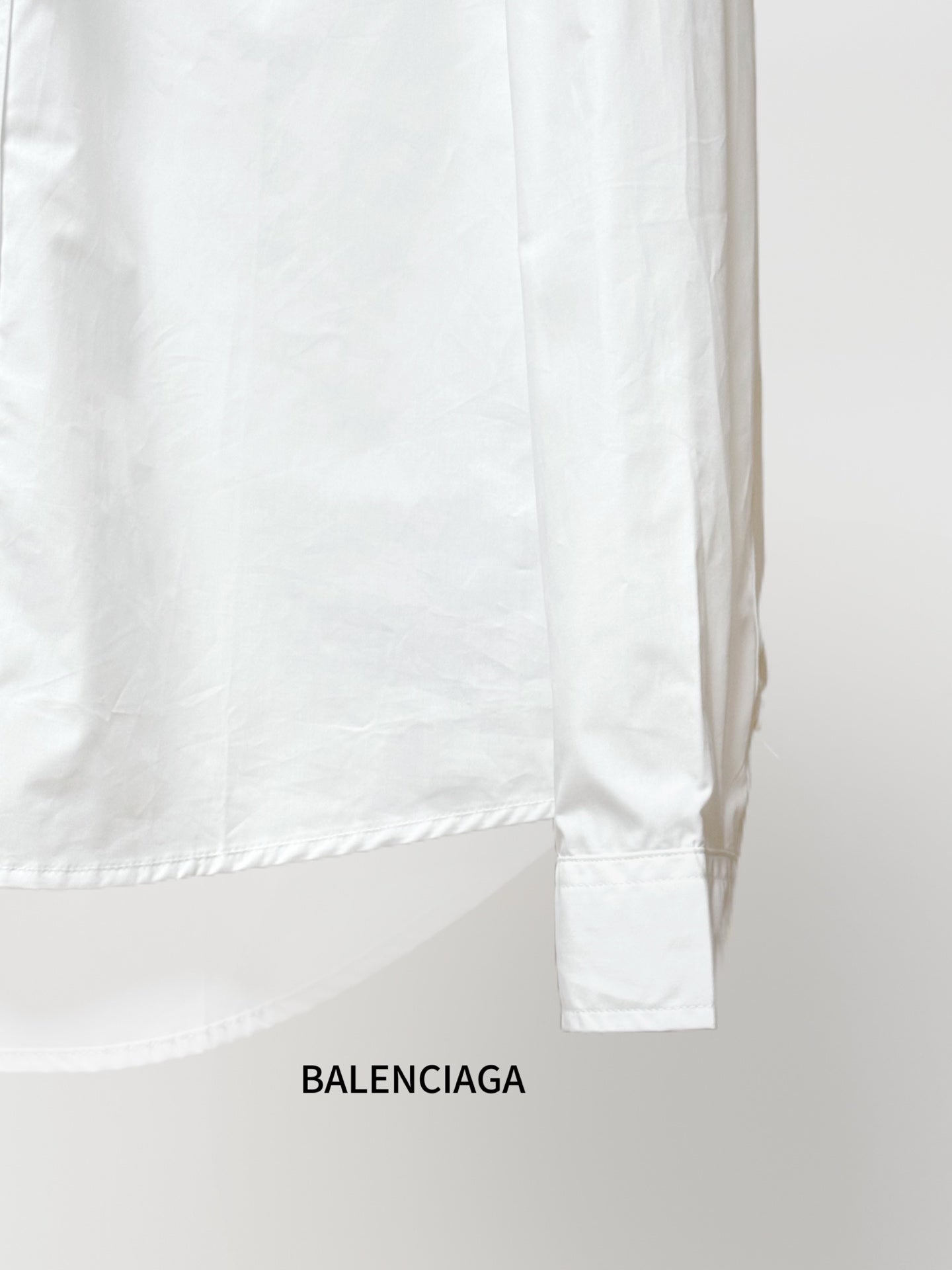 Balenciaga long-sleeve shirt lower back, white fabric with curved hem and sleeve cuff.