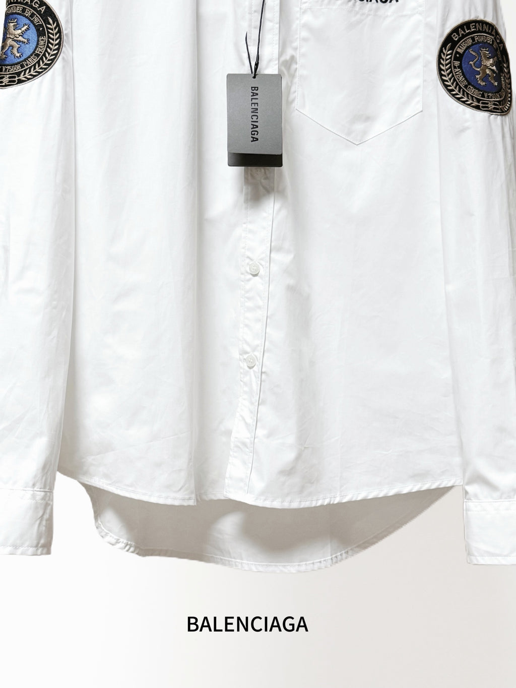 Balenciaga long-sleeve shirt close-up, white front with tag and chest pocket; sleeve patches.