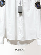 Balenciaga long-sleeve shirt close-up, white front with tag and chest pocket; sleeve patches.