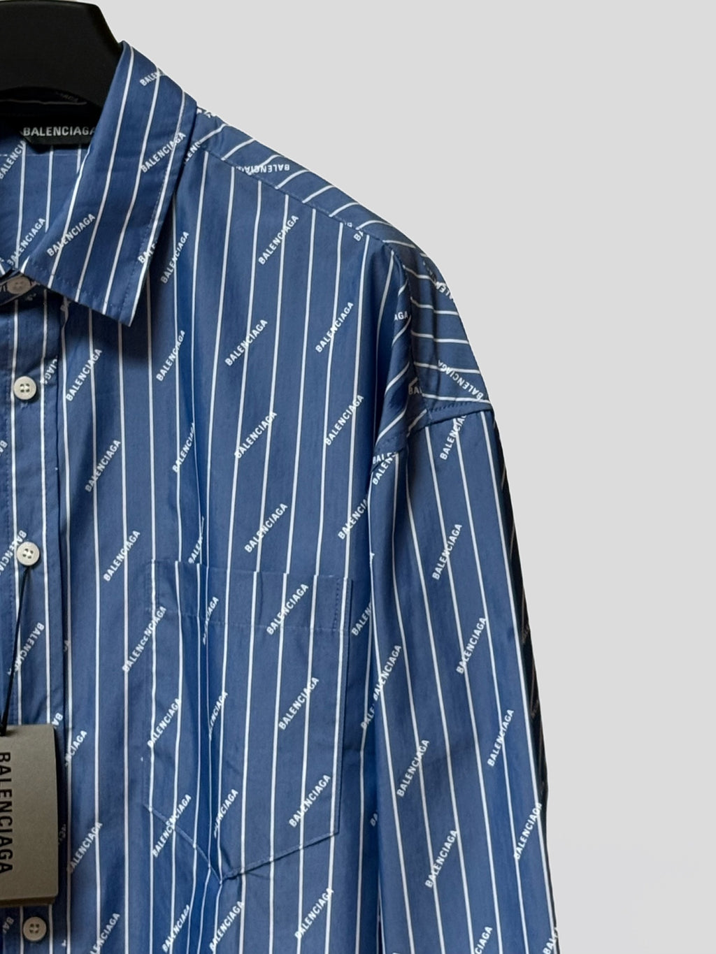 Blue button-up shirt shoulder with vertical pinstripe logo print and button cuff
