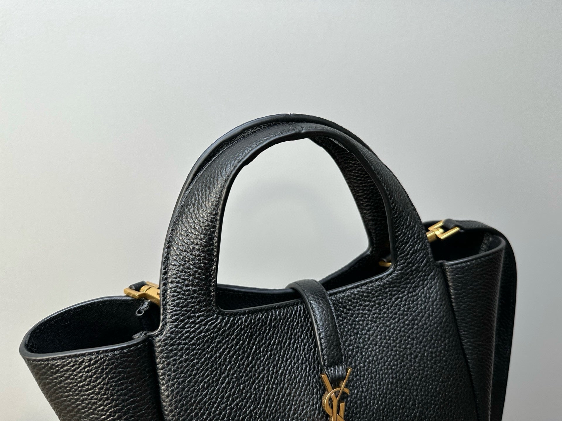 YSL tote bag close-up showing textured leather, handle opening, and gold charm on strap
