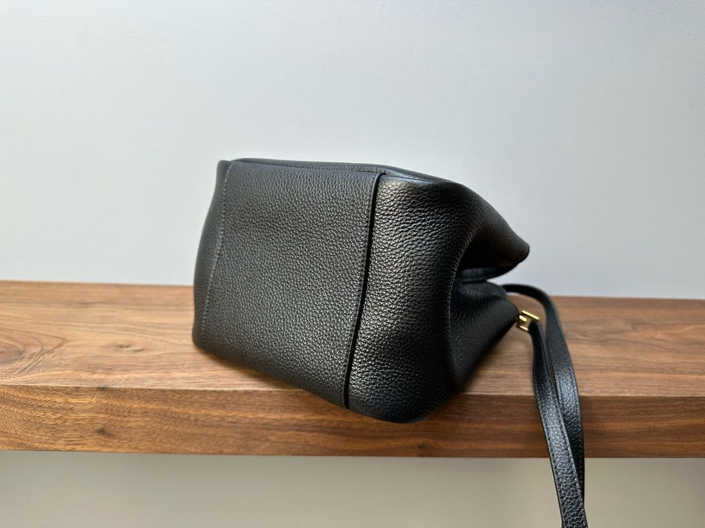 Black leather mini handbag back view with strap, curved seams and gold-tone hardware