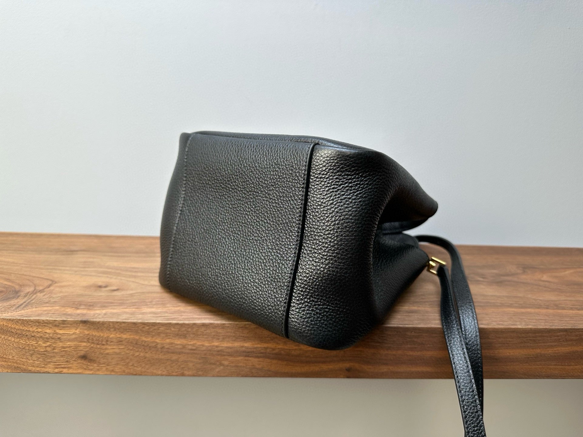 Black leather mini handbag back view with strap, curved seams and gold-tone hardware