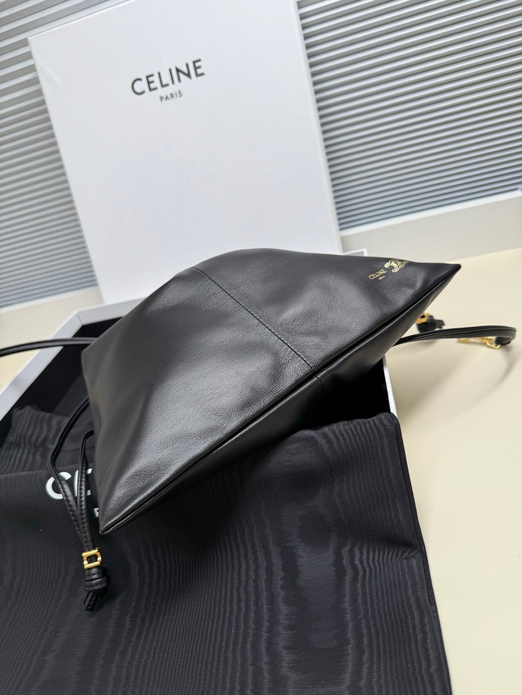 Black leather drawstring bag side view with gold-toned logo and strap hardware
