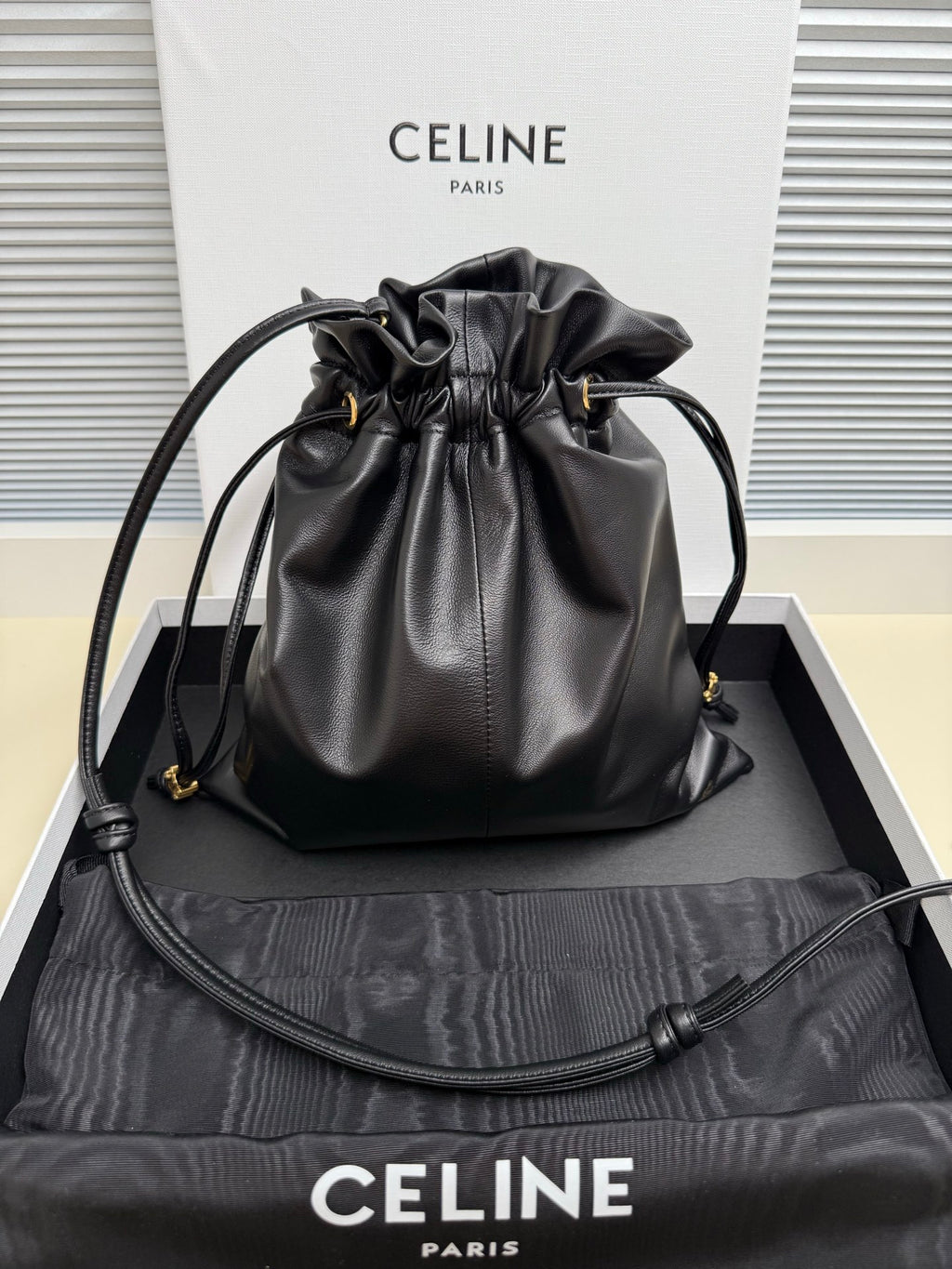Black leather drawstring bag with gold-toned logo and adjustable shoulder strap