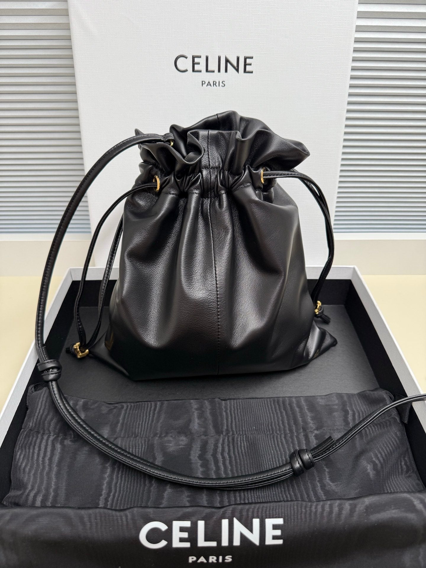 Black leather drawstring bag with gold-toned logo and adjustable shoulder strap