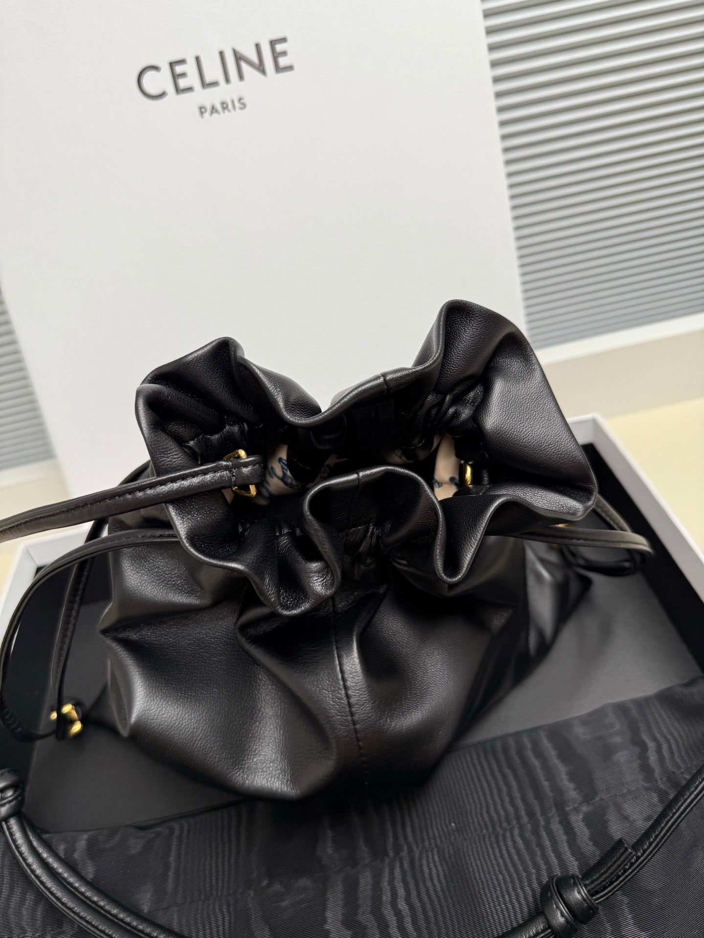 Black leather drawstring bag with gathered top and gold-toned eyelets