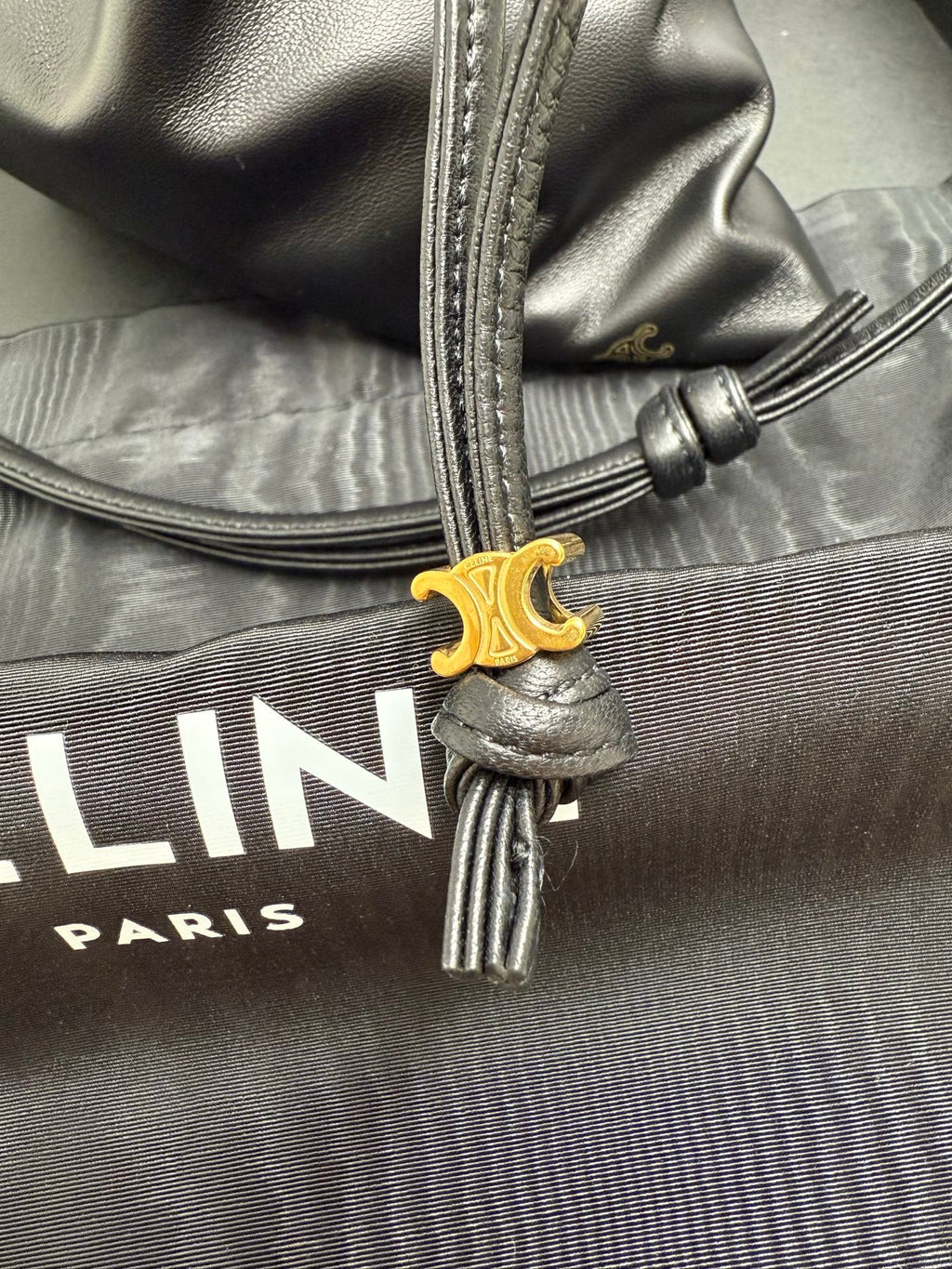 Black leather drawstring bag with gold-tone logo charm and stitched strap ends