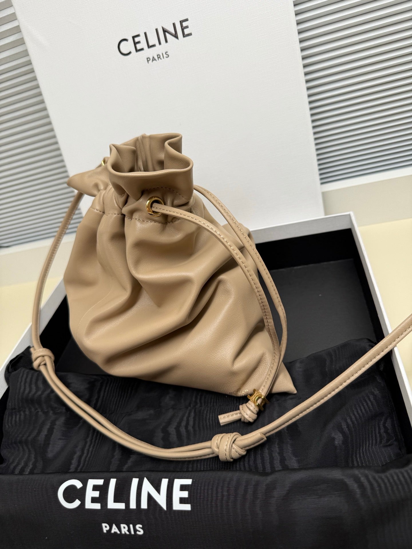 Beige leather drawstring pouch bag with gathered top and crossbody braided strap
