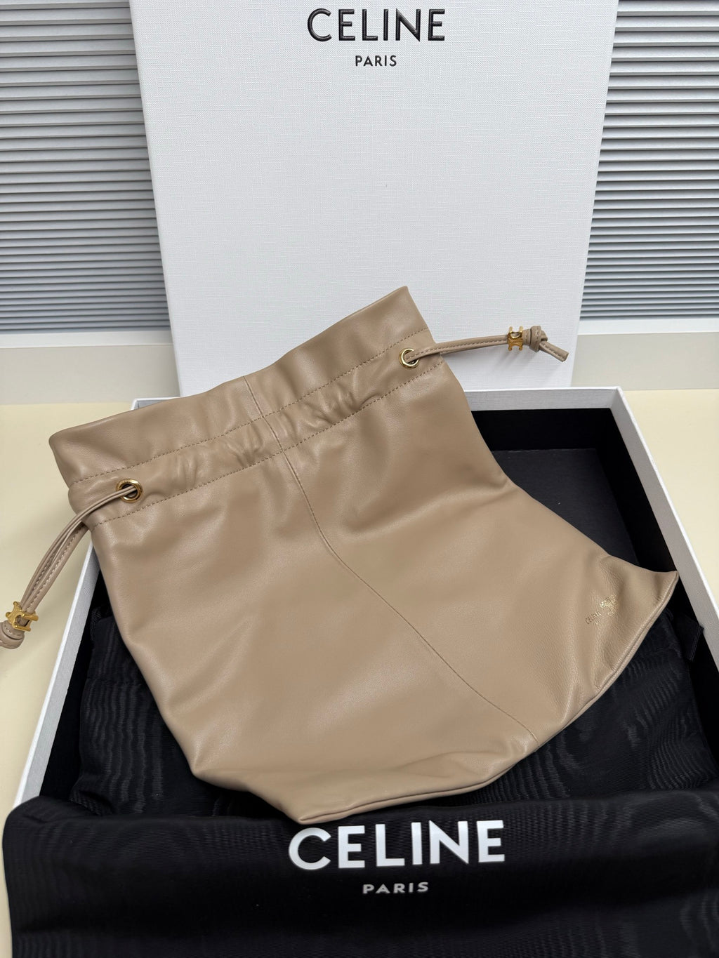 Beige leather pouch with front seam, two handles, and small metal hardware accents
