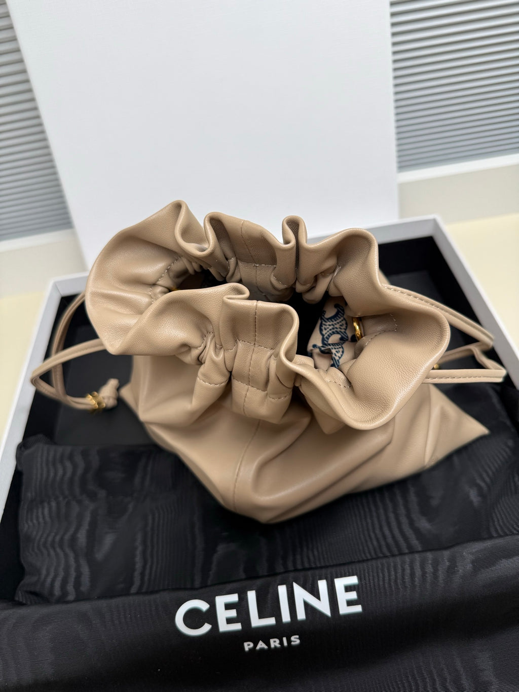 Beige leather drawstring pouch bag with open top and visible patterned interior lining