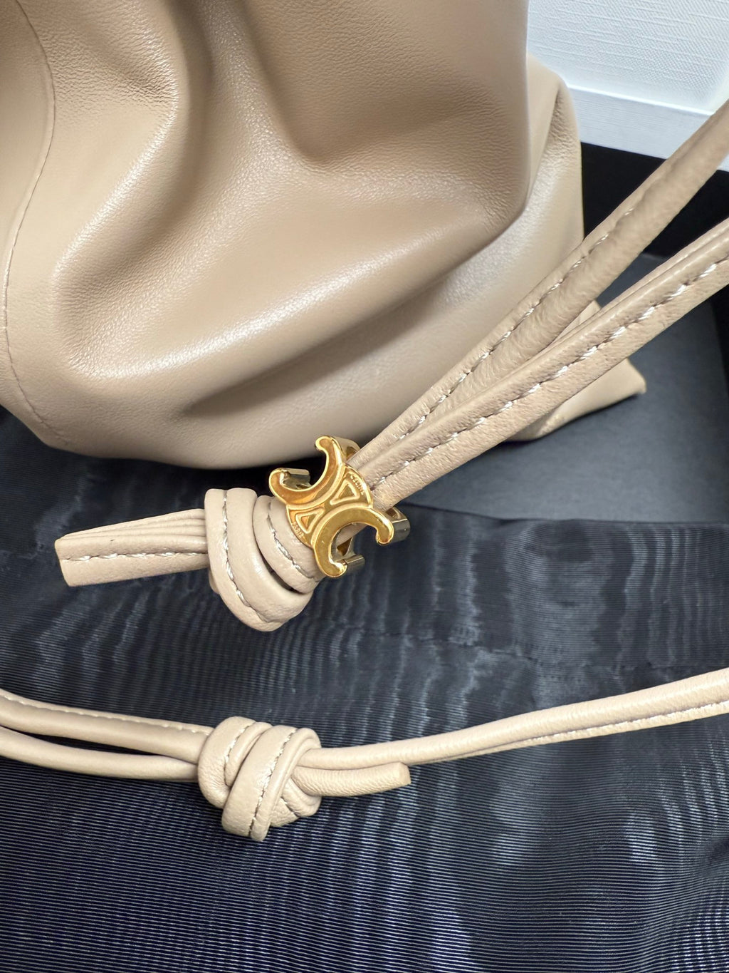 Beige leather drawstring pouch close-up with gold tone toggle clasp and braided cord