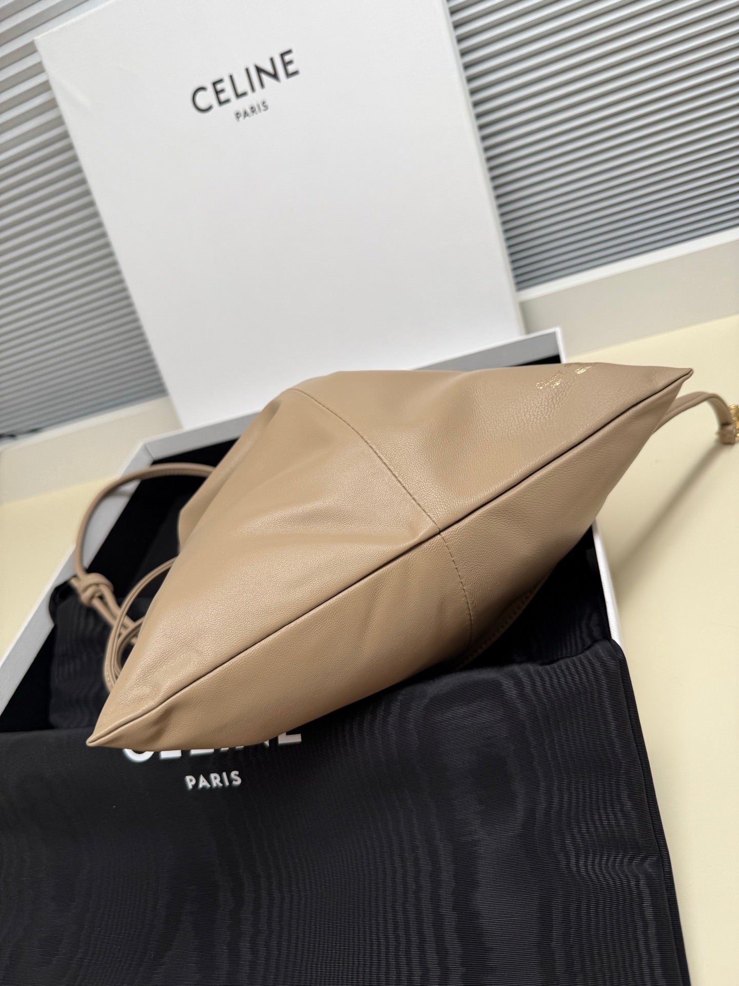 Beige leather drawstring pouch bag side view with diagonal seam and braided handle