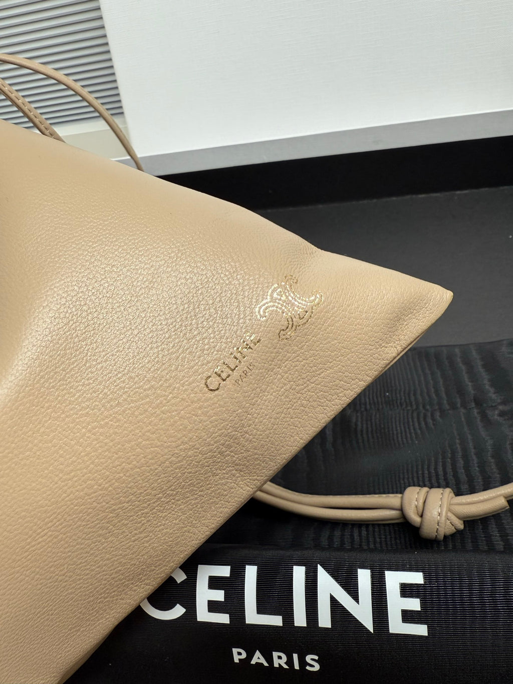 Beige leather pouch with embossed logo detail and braided cord strap attachment