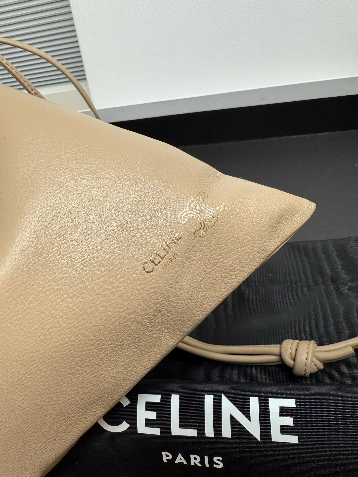 Beige leather pouch with embossed logo detail and braided cord strap attachment