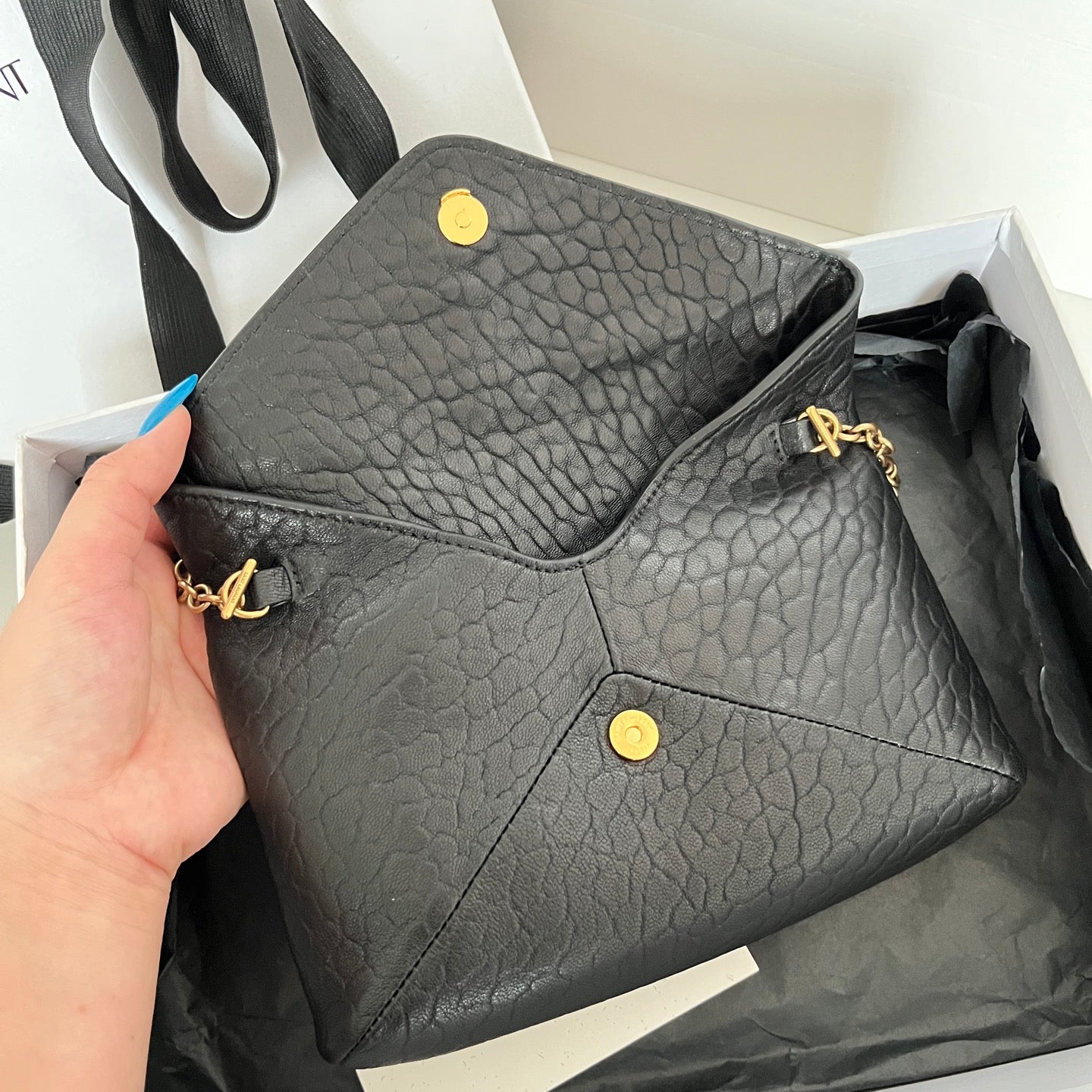 Black textured leather YSL crossbody bag with gold snap buttons, held in hand